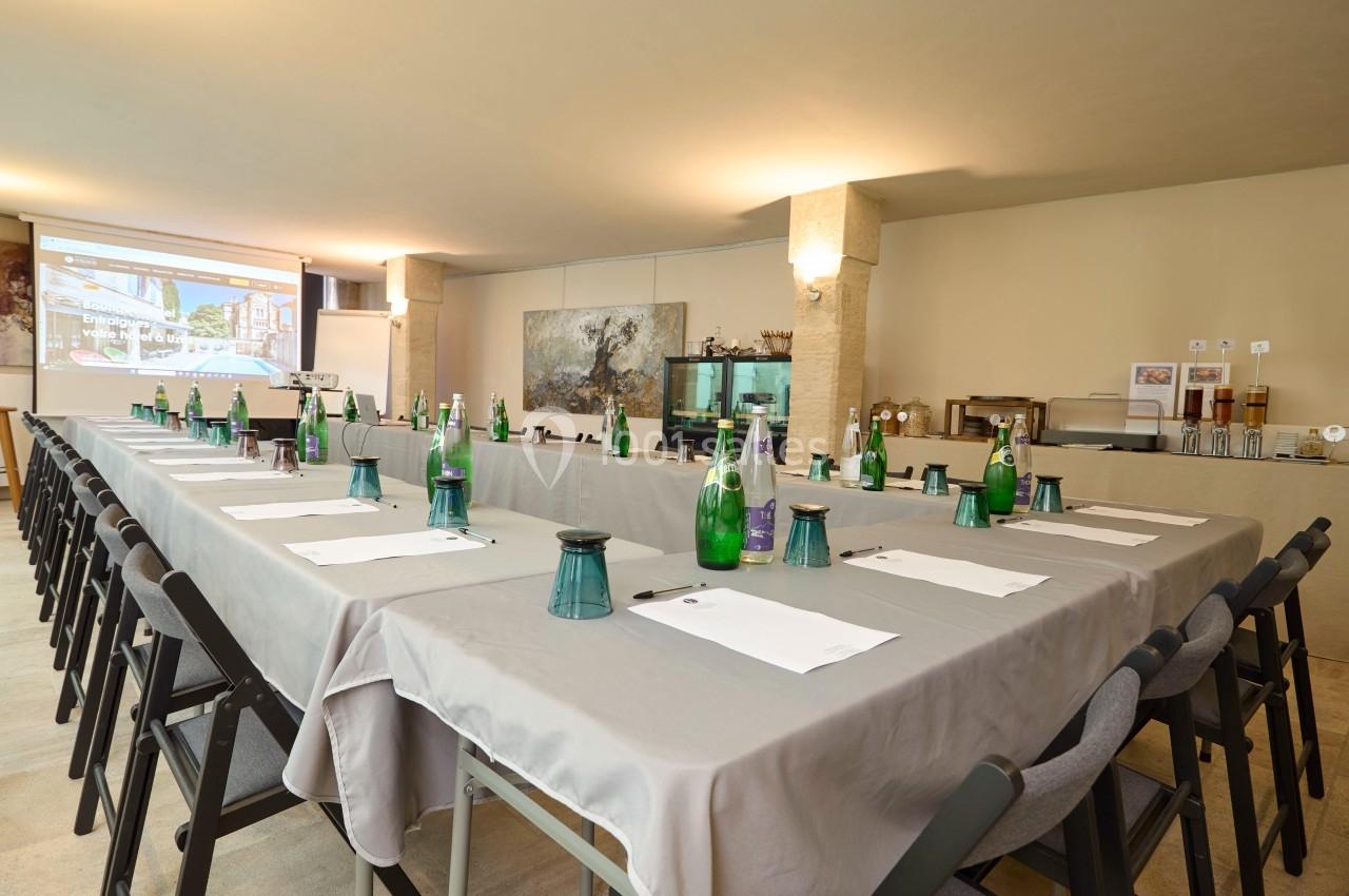 Salle de réunion aménagée avec une grande table en U, chaises, bouteilles d'eau, blocs-notes et écran de projection.