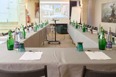 Salle de réunion avec tables disposées en U, chaises noires, bouteilles d'eau et écran de projection allumé.