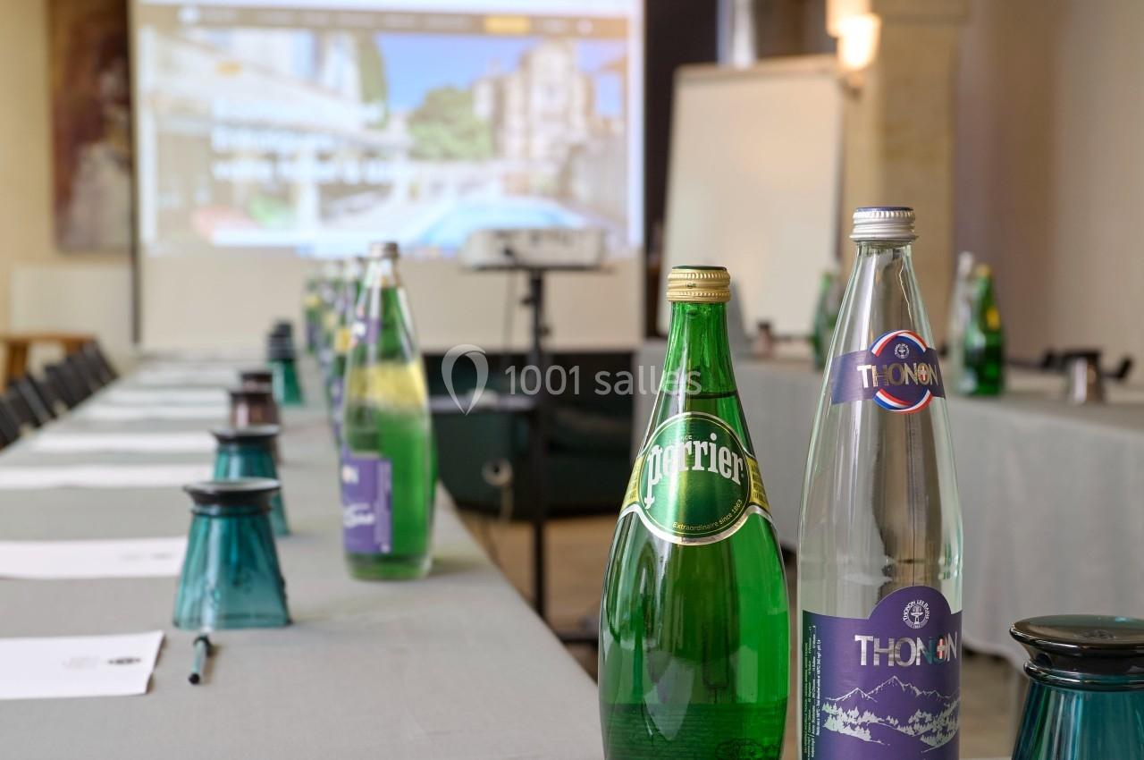 Bouteilles d'eau minérale posées sur une table de réunion avec écran de présentation flou en arrière-plan.