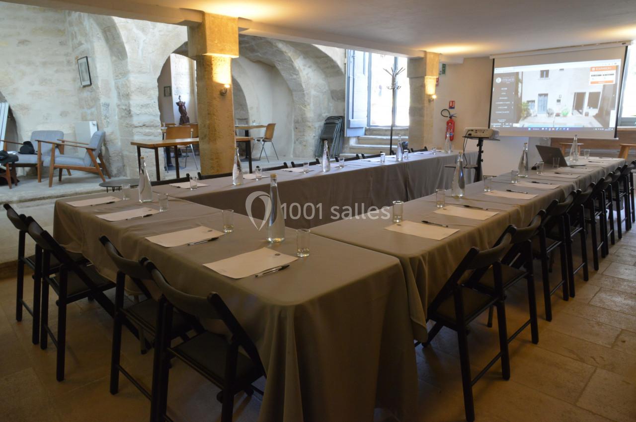 Salle de réunion avec tables disposées en U, chaises noires, projecteur et lumière naturelle.
