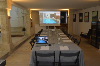 Salle de réunion avec tables disposées en U, chaises noires, bouteilles d'eau et écran de projection allumé.