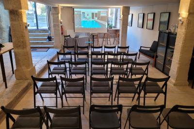 Salle de réunion avec tables disposées en U, chaises noires, bouteilles d'eau et écran de projection allumé.