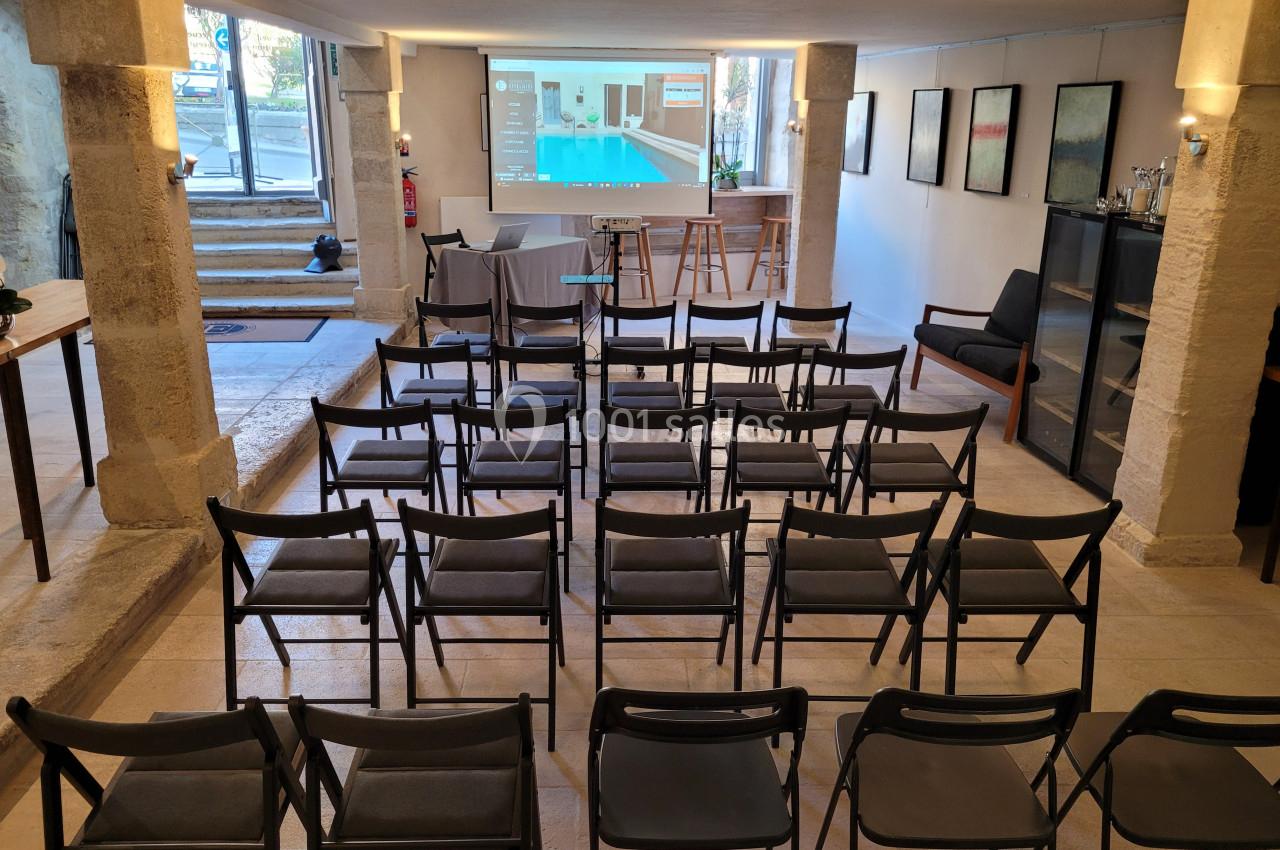 Salle de réunion avec des chaises alignées face à un écran de projection, éclairée par une lumière naturelle et artificielle.
