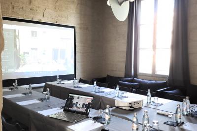 Salle de réunion avec tables disposées en U, chaises noires, bouteilles d'eau et écran de projection allumé.