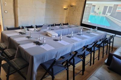Salle de réunion avec tables disposées en U, chaises noires, bouteilles d'eau et écran de projection allumé.