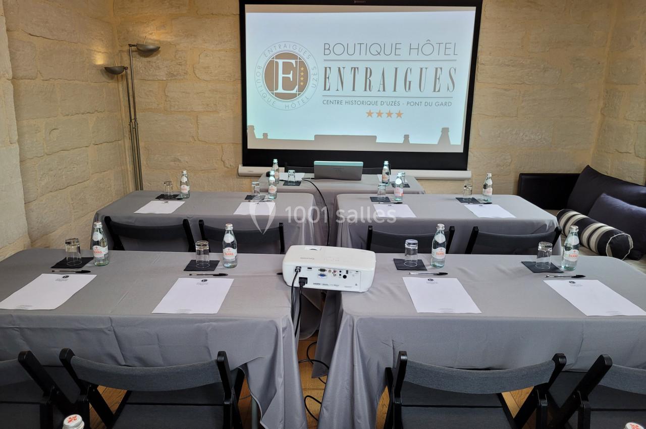 Salle de réunion équipée avec tables, chaises, projecteur, bouteilles d'eau et écran affichant le logo d'un hôtel.