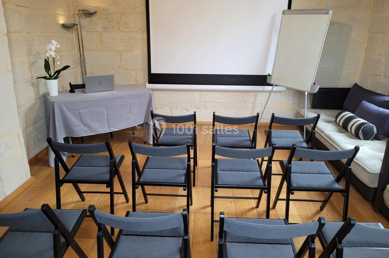 Salle de réunion équipée de chaises pliantes, d'un écran de projection, d'un tableau blanc et d'une table avec ordinateur.