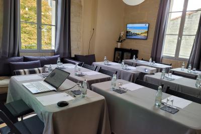 Salle de réunion avec tables disposées en U, chaises noires, bouteilles d'eau et écran de projection allumé.