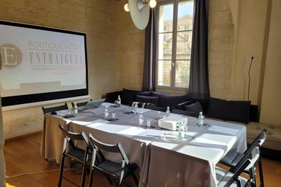 Salle de réunion avec tables disposées en U, chaises noires, bouteilles d'eau et écran de projection allumé.