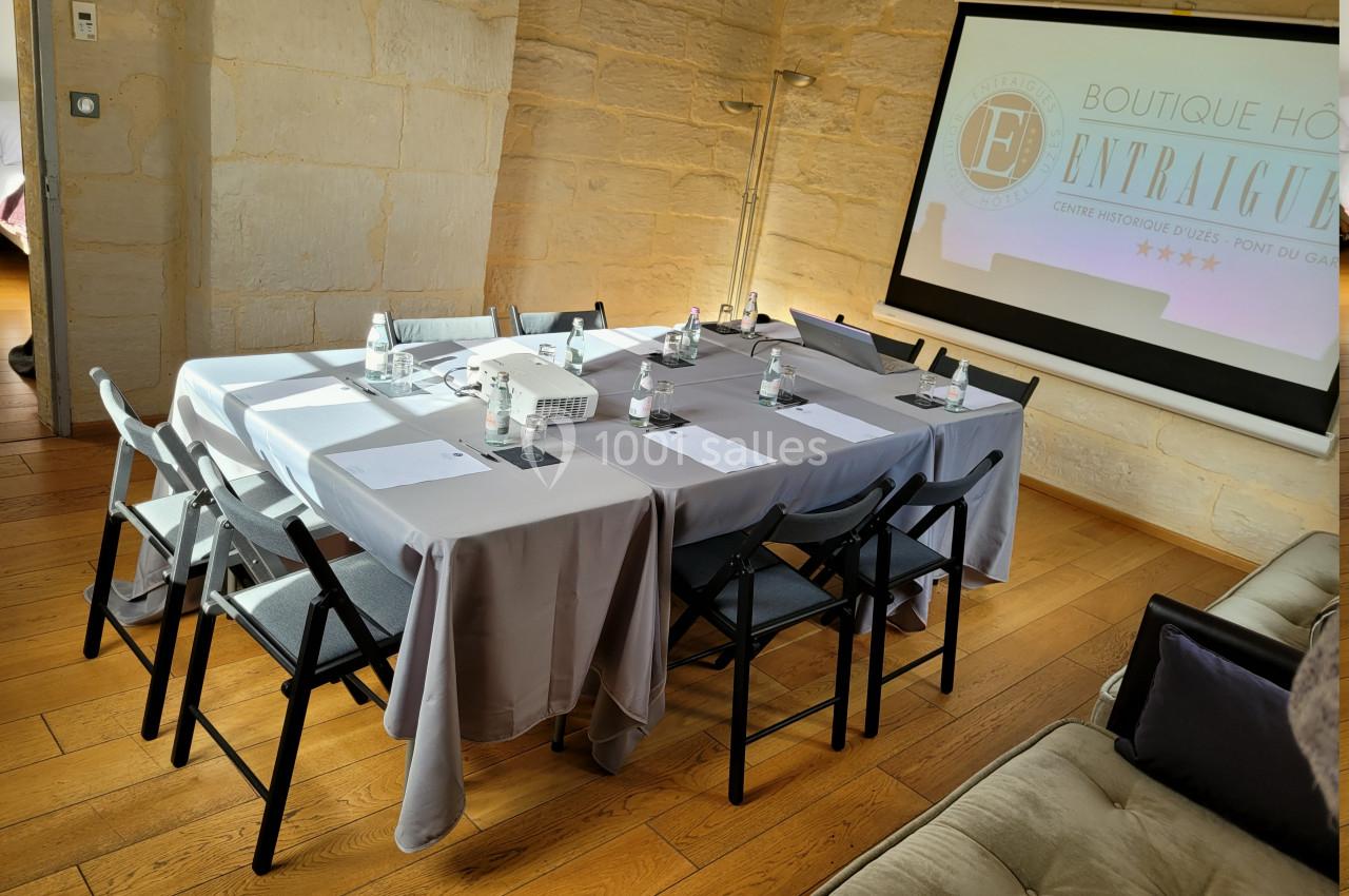 Salle de réunion lumineuse avec table rectangulaire dressée, chaises pliantes, projecteur et écran de présentation.
