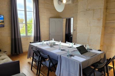 Salle de réunion avec tables disposées en U, chaises noires, bouteilles d'eau et écran de projection allumé.