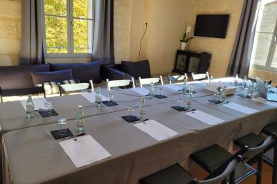 Salle de réunion avec tables disposées en U, chaises noires, bouteilles d'eau et écran de projection allumé.