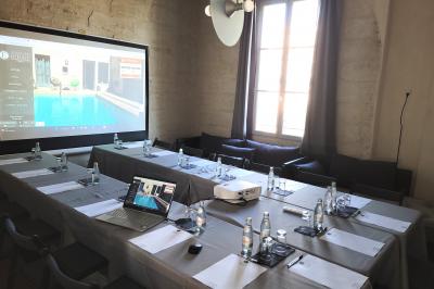 Salle de réunion avec tables disposées en U, chaises noires, bouteilles d'eau et écran de projection allumé.