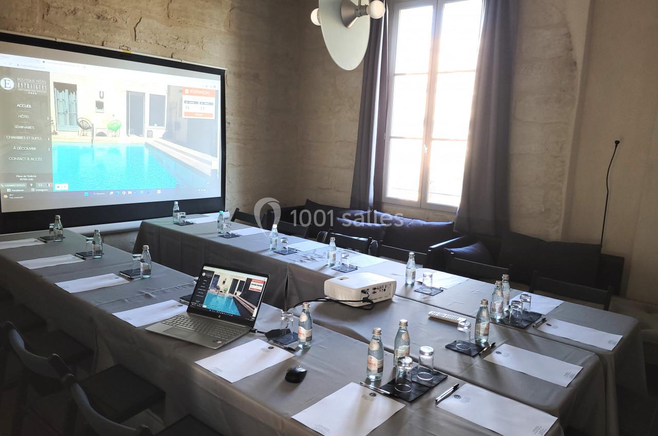 Salle de réunion équipée avec projecteur, ordinateur portable et documents disposés sur des tables en U.