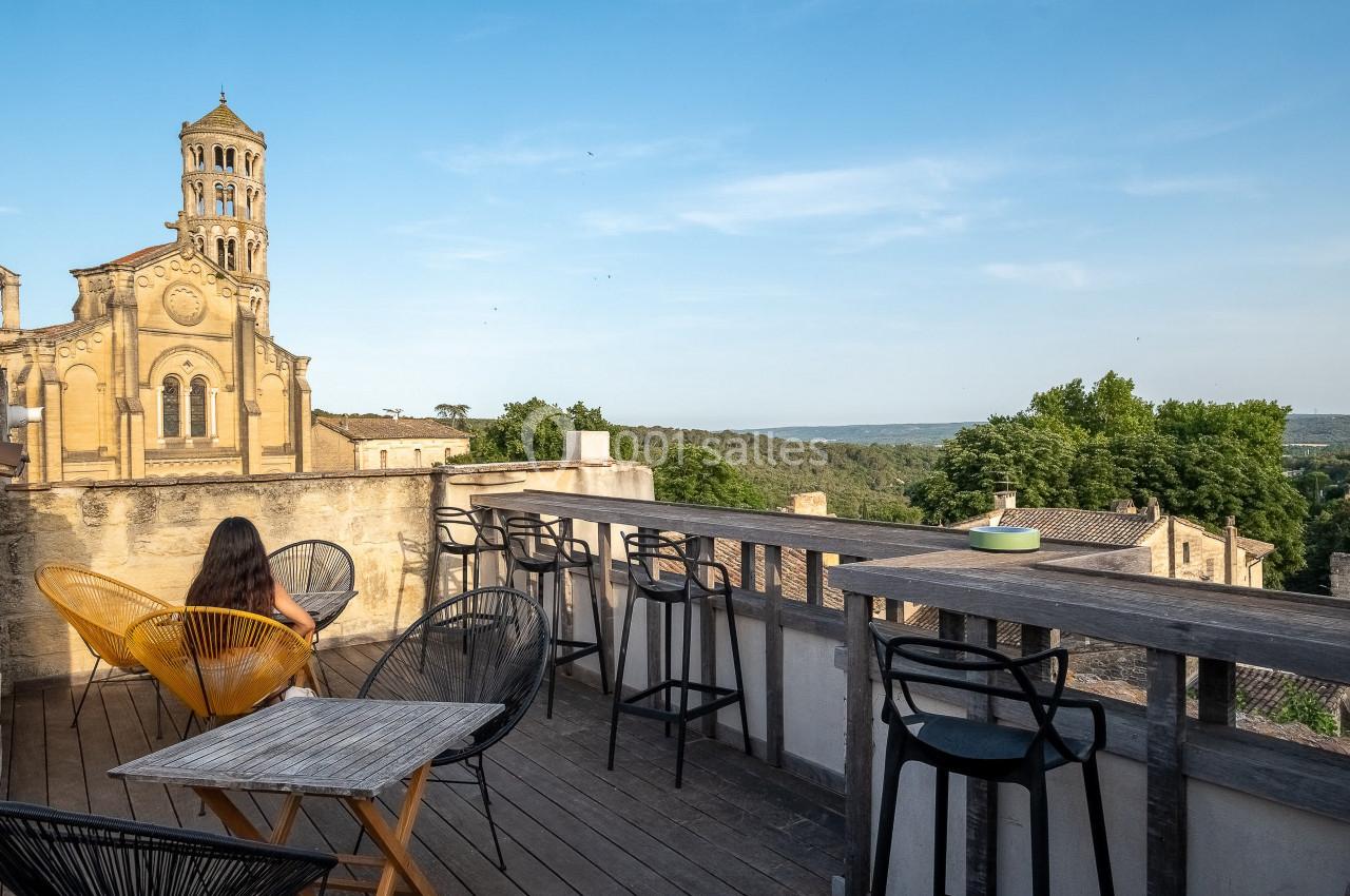 Terrasse avec vue sur une église ancienne, des collines verdoyantes et des chaises modernes en premier plan.