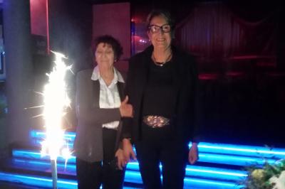 Salle de réception décorée avec des guirlandes et des lumières colorées, des invités assis et dansant.