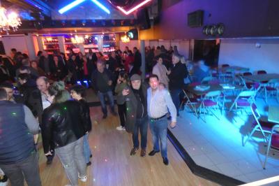 Salle de réception décorée avec des guirlandes et des lumières colorées, des invités assis et dansant.