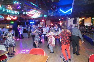 Salle de réception décorée avec des guirlandes et des lumières colorées, des invités assis et dansant.