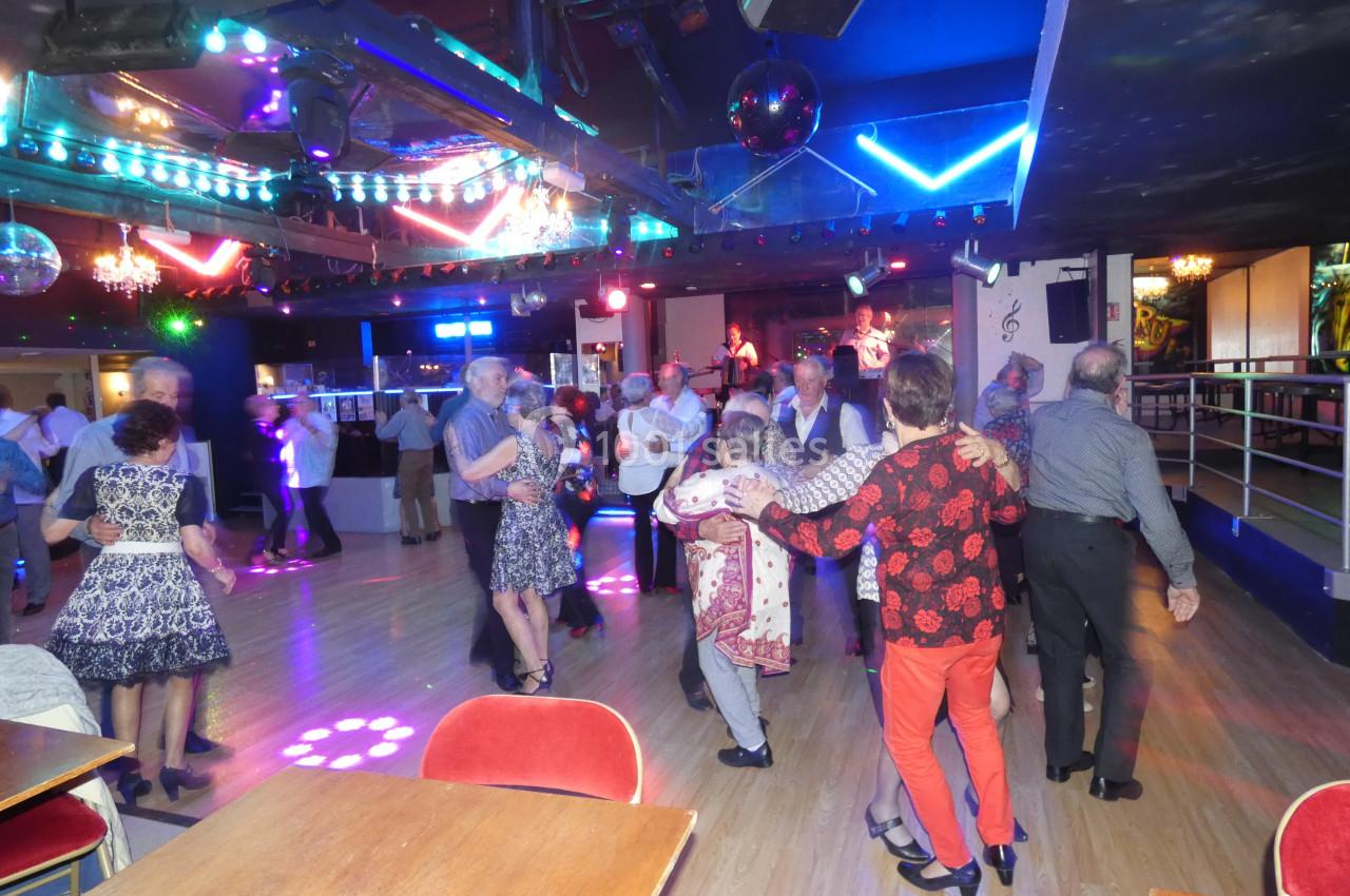 Personnes dansant sur une piste éclairée par des lumières colorées dans une salle festive.