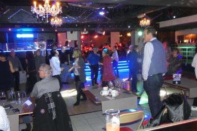 Salle de réception décorée avec des guirlandes et des lumières colorées, des invités assis et dansant.