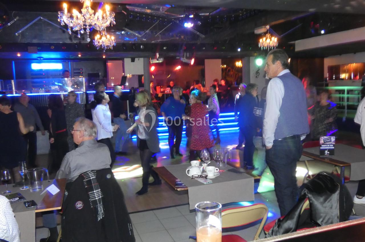 Des personnes dansent et discutent dans une salle animée avec éclairages colorés et ambiance festive.