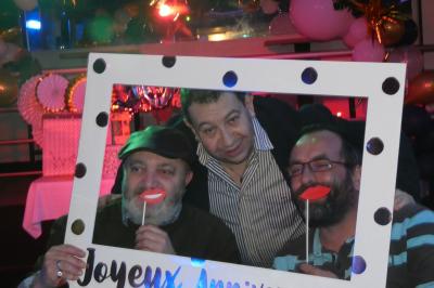 Salle de réception décorée avec des guirlandes et des lumières colorées, des invités assis et dansant.