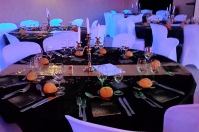 Salle de réception décorée avec des guirlandes et des lumières colorées, des invités assis et dansant.