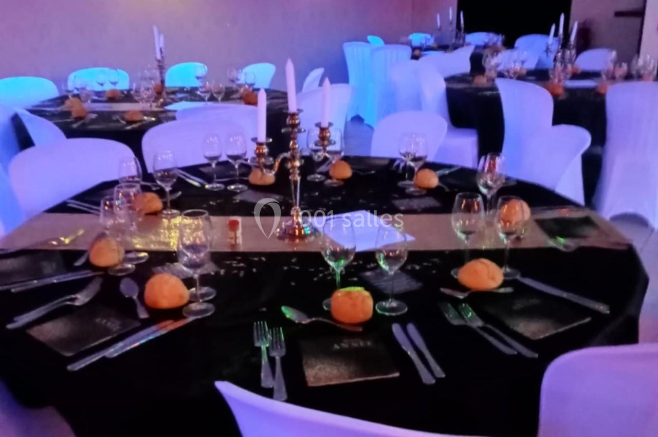 Salle de réception décorée avec des tables rondes, nappes noires, bougeoirs dorés et petites citrouilles en centre de table.