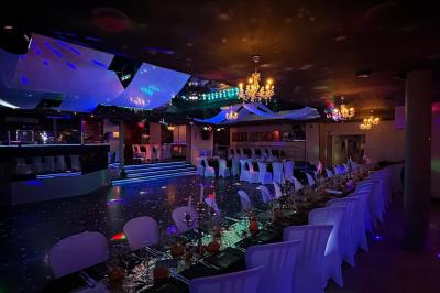 Salle de réception décorée avec des guirlandes et des lumières colorées, des invités assis et dansant.