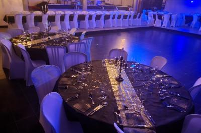 Salle de réception décorée avec des guirlandes et des lumières colorées, des invités assis et dansant.