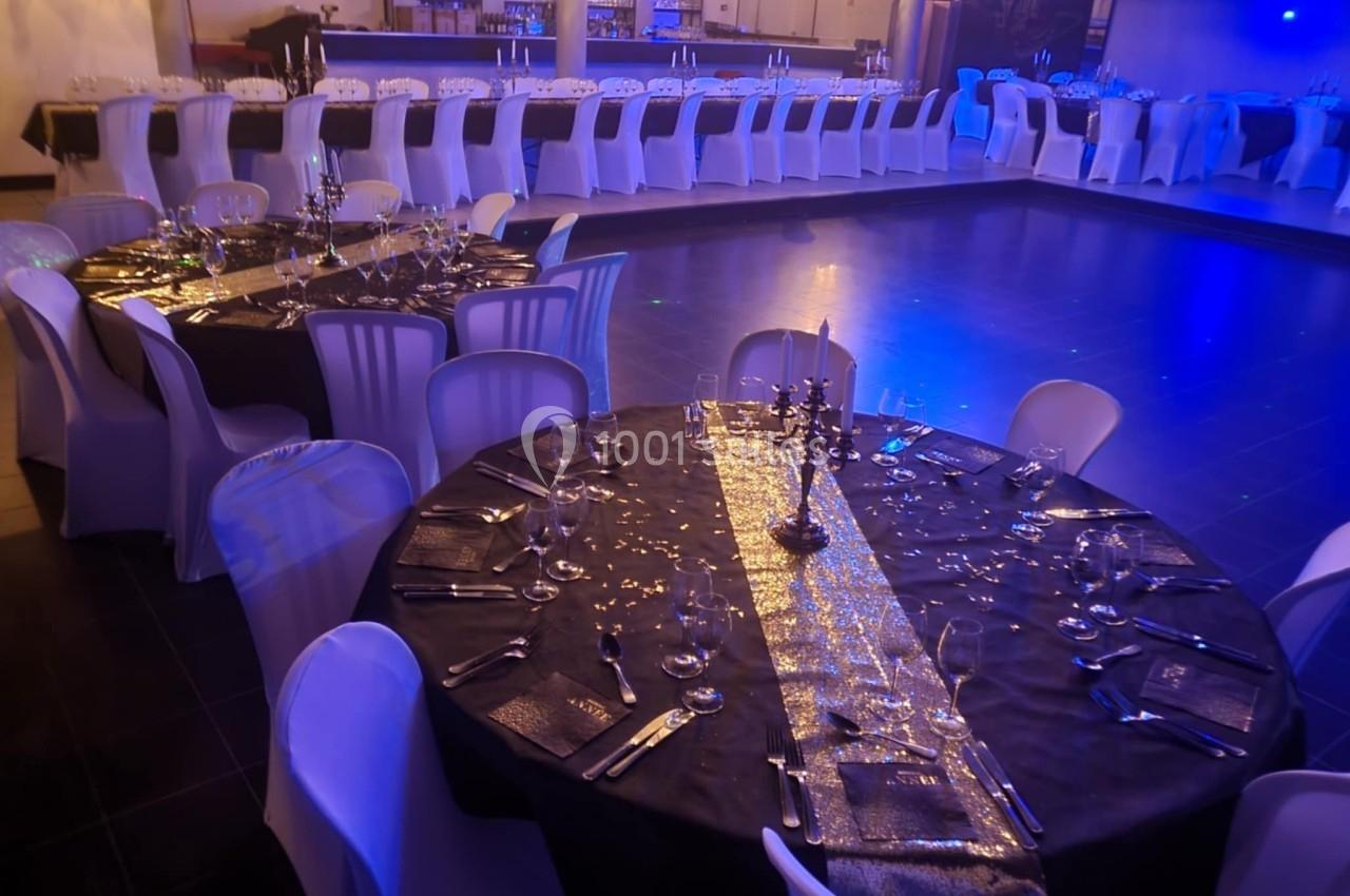 Salle de réception décorée avec des tables rondes et rectangulaires, nappes noires, couverts élégants et éclairage tamisé.