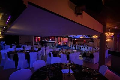 Salle de réception décorée avec des guirlandes et des lumières colorées, des invités assis et dansant.