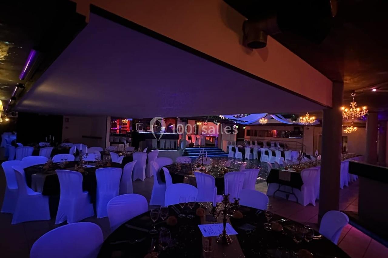 Salle de réception décorée avec des tables rondes, nappes noires, chaises blanches et éclairage tamisé.