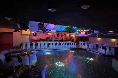 Salle de réception décorée avec des guirlandes et des lumières colorées, des invités assis et dansant.