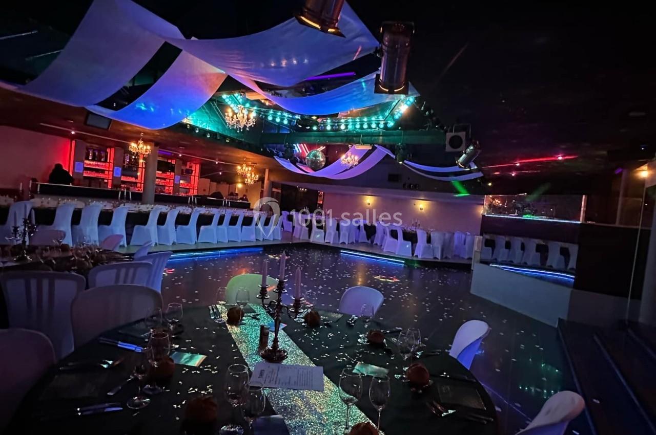 Salle de réception décorée avec des tables dressées, piste de danse illuminée et éclairages colorés au plafond.