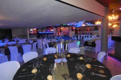 Salle de réception décorée avec des guirlandes et des lumières colorées, des invités assis et dansant.