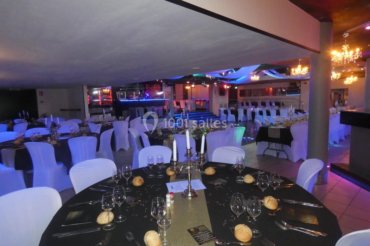 Salle de réception décorée avec des tables dressées, nappes noires et blanches, chandeliers et éclairage coloré.