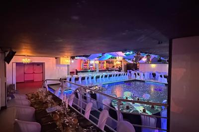 Salle de réception décorée avec des guirlandes et des lumières colorées, des invités assis et dansant.