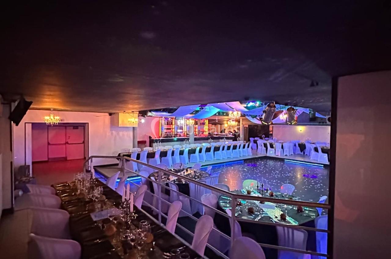 Salle de réception élégante avec tables dressées, éclairage tamisé et vue sur une piscine illuminée.