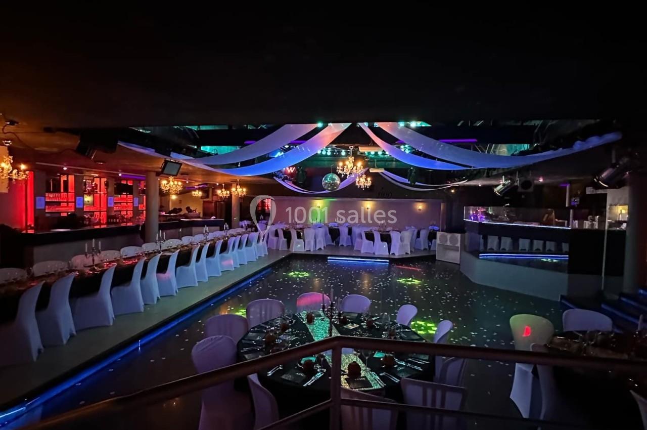 Salle de réception décorée avec des tables dressées, des chaises blanches et un éclairage tamisé coloré.