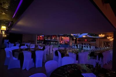 Salle de réception décorée avec des guirlandes et des lumières colorées, des invités assis et dansant.