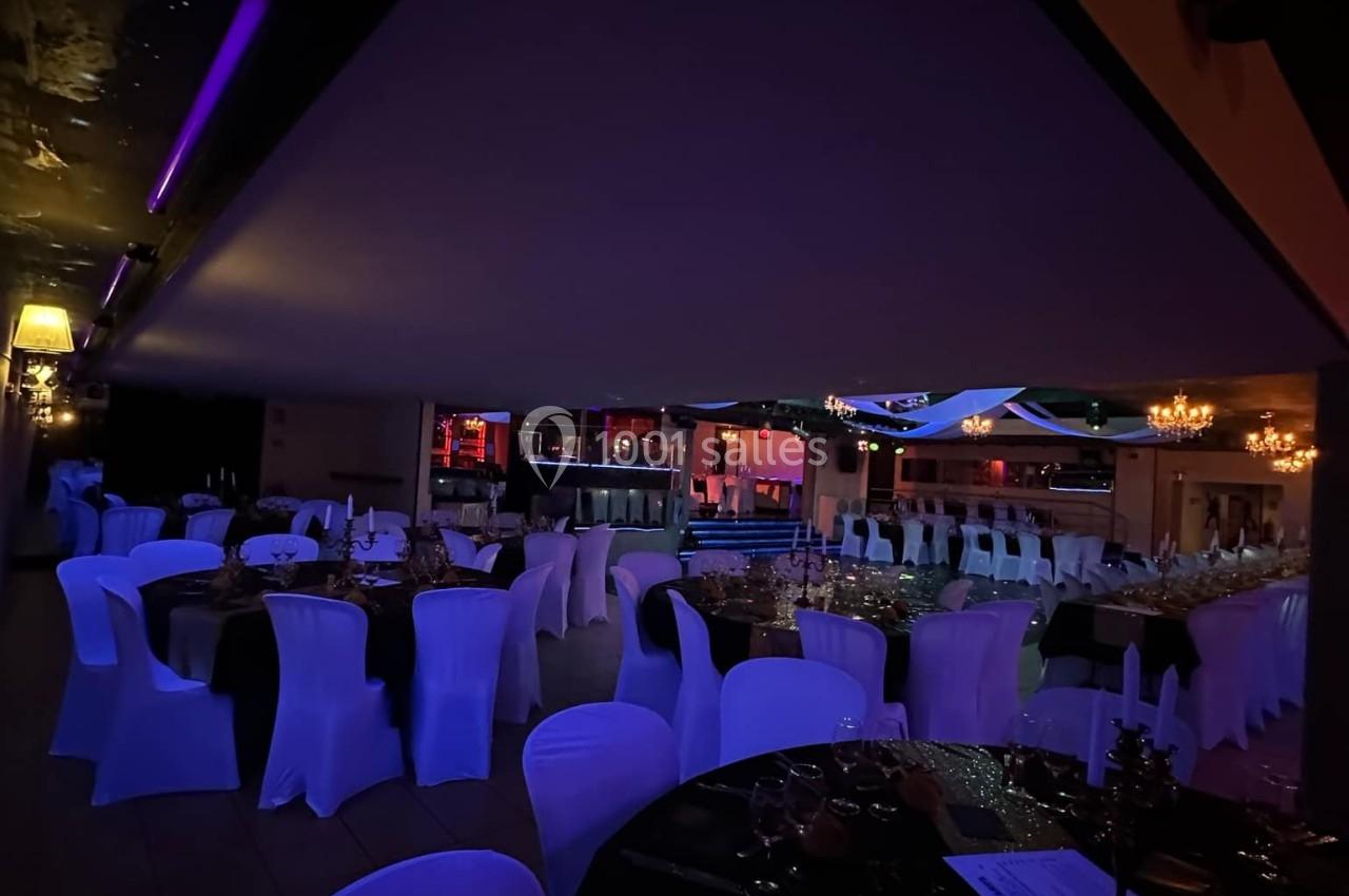 Salle de réception faiblement éclairée, avec des tables dressées et des chaises couvertes de housses blanches.