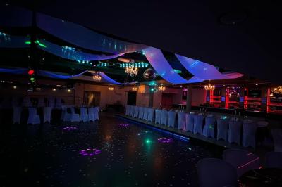 Salle de réception décorée avec des guirlandes et des lumières colorées, des invités assis et dansant.