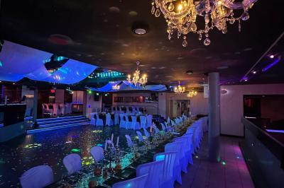 Salle de réception décorée avec des guirlandes et des lumières colorées, des invités assis et dansant.