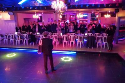 Salle de réception décorée avec des guirlandes et des lumières colorées, des invités assis et dansant.