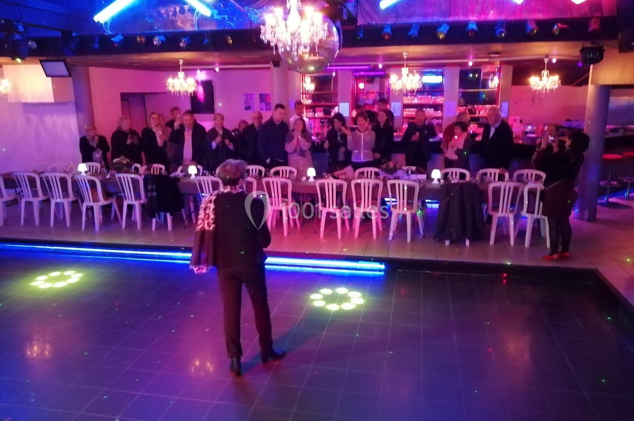 Un animateur s'adresse à un public debout et assis dans une salle éclairée par des lumières colorées.