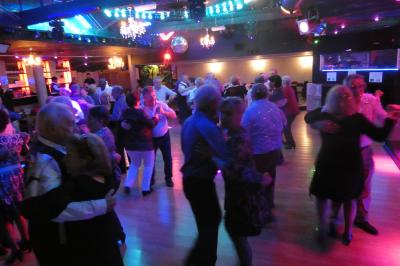 Salle de réception décorée avec des guirlandes et des lumières colorées, des invités assis et dansant.