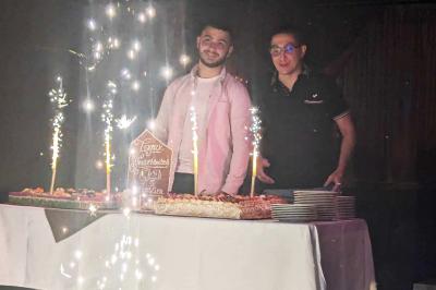Salle de réception décorée avec des guirlandes et des lumières colorées, des invités assis et dansant.