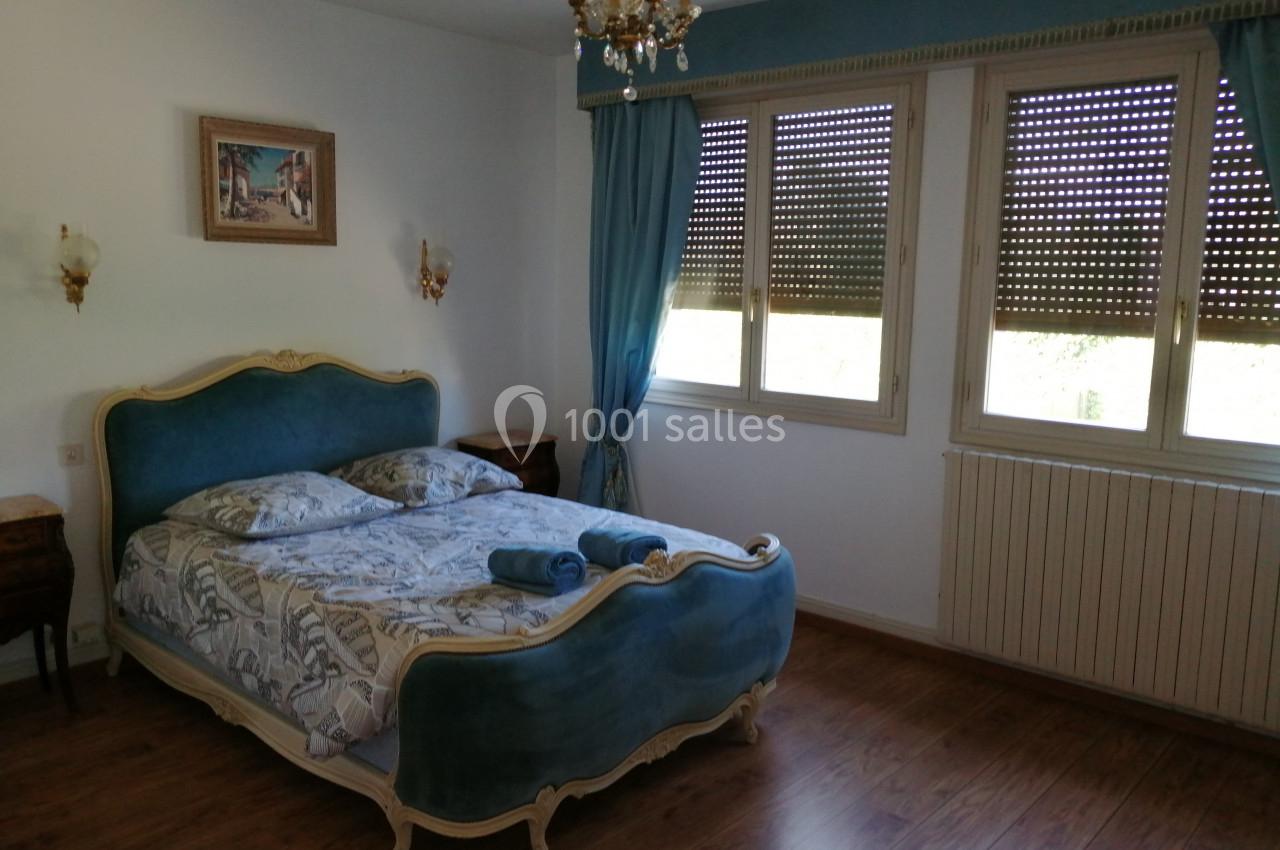 Chambre lumineuse avec lit double à tête de lit bleue, rideaux assortis, parquet et décoration classique.