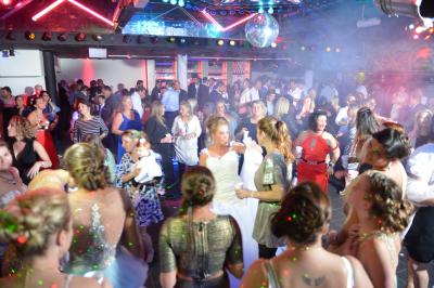 Salle de réception décorée avec des guirlandes et des lumières colorées, des invités assis et dansant.